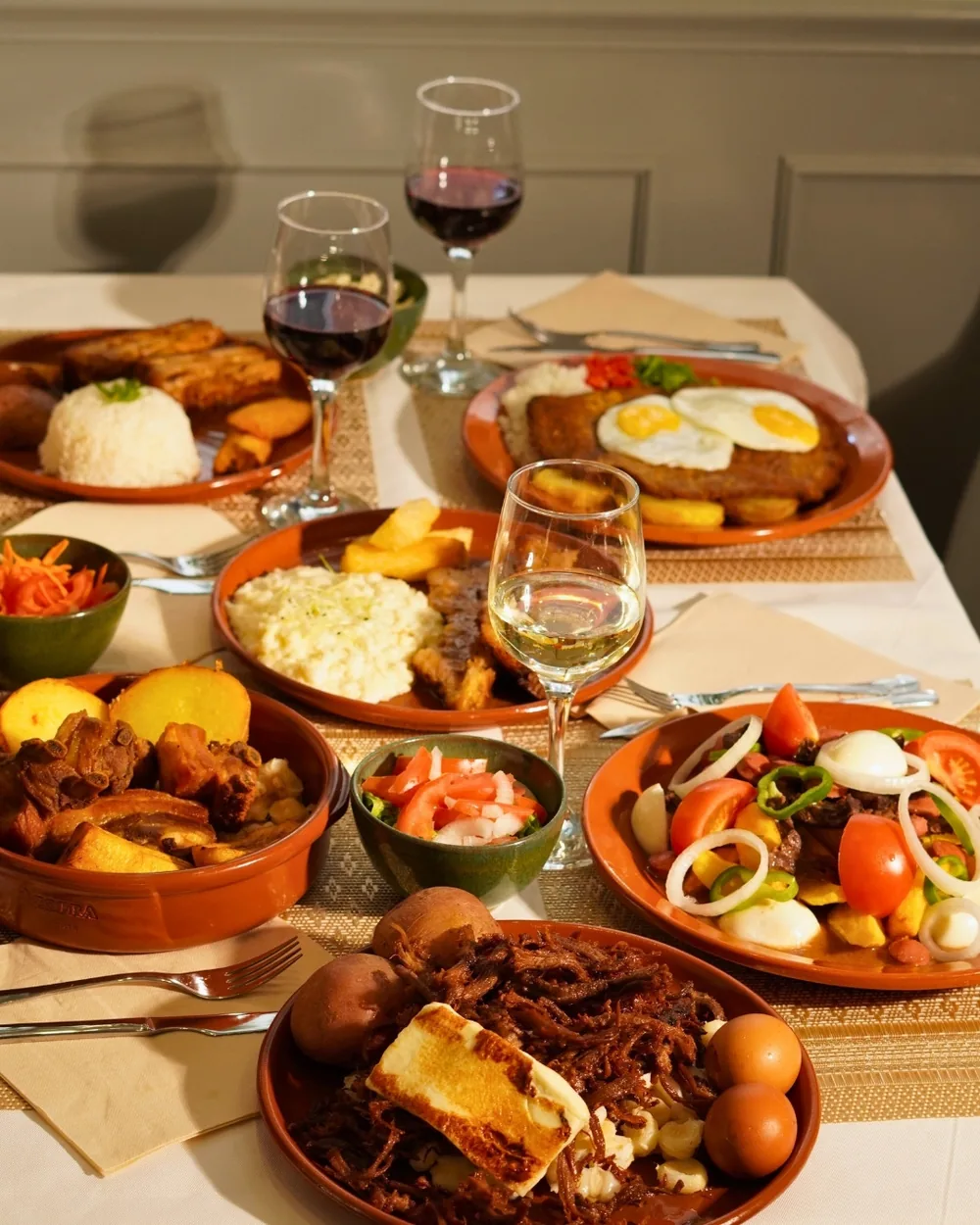 A table in the dining room with several Bolivian dishes on clay plates and glasses of wine
