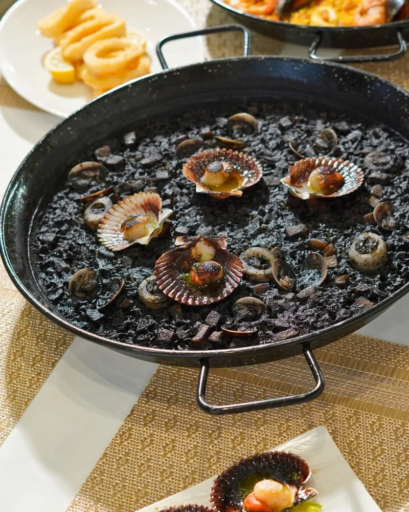 Un arroz negro con zamburiñas en su paella, sobre la mesa