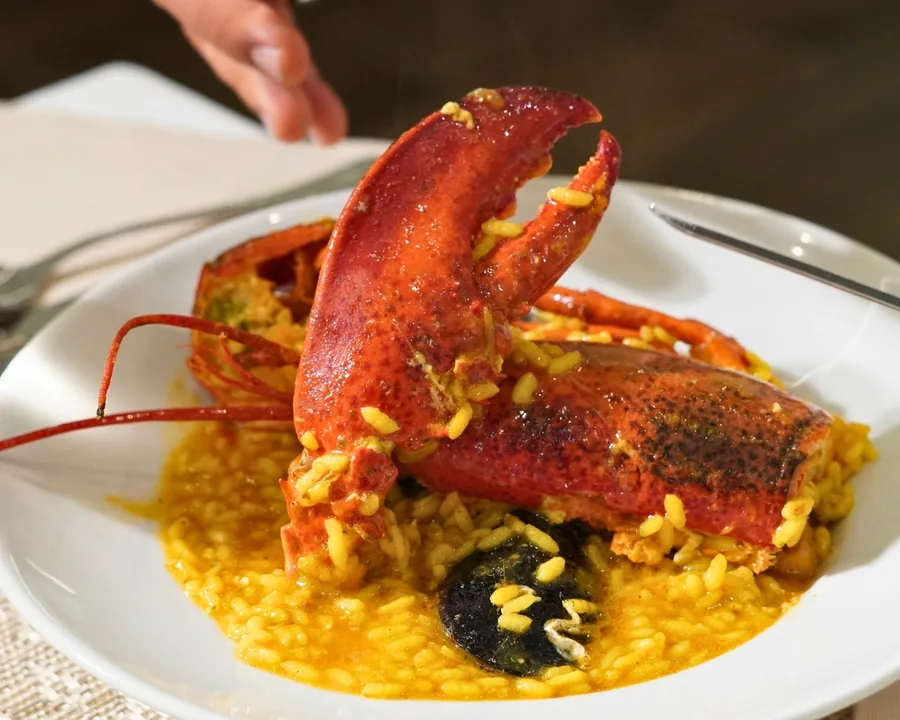Medio bogavante sobre el arroz caldoso, servido en un plato hondo