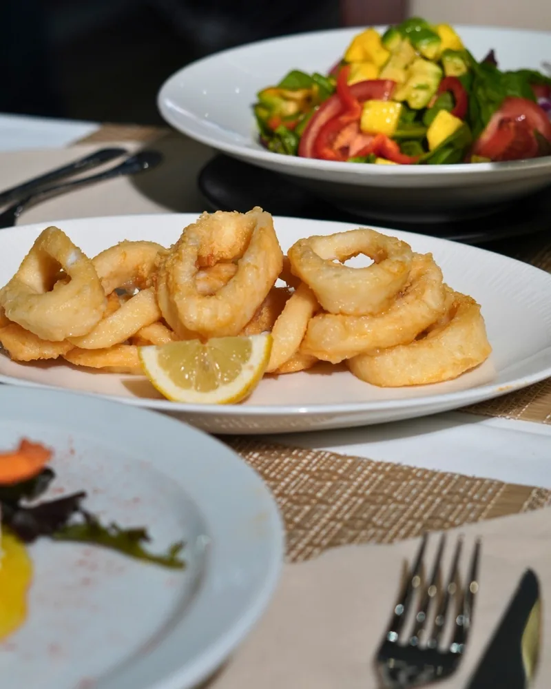 Un plato de calamares a la andaluza con limón y, detrás, una ensalada