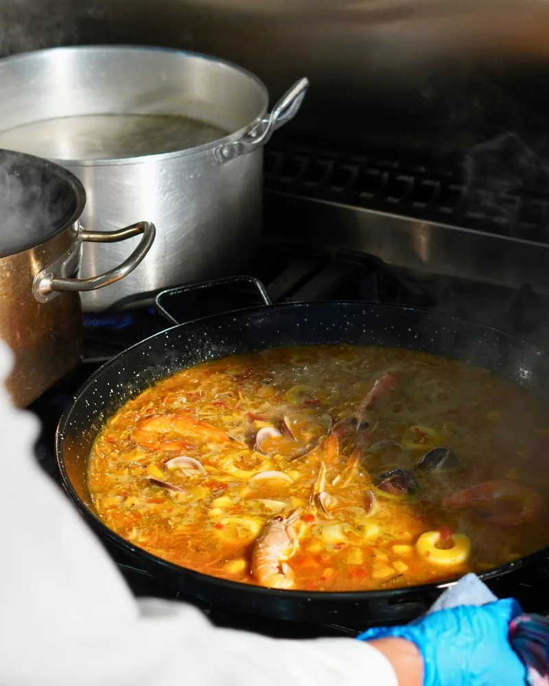 Una paella al fuego en la cocina, con el caldo y el marisco