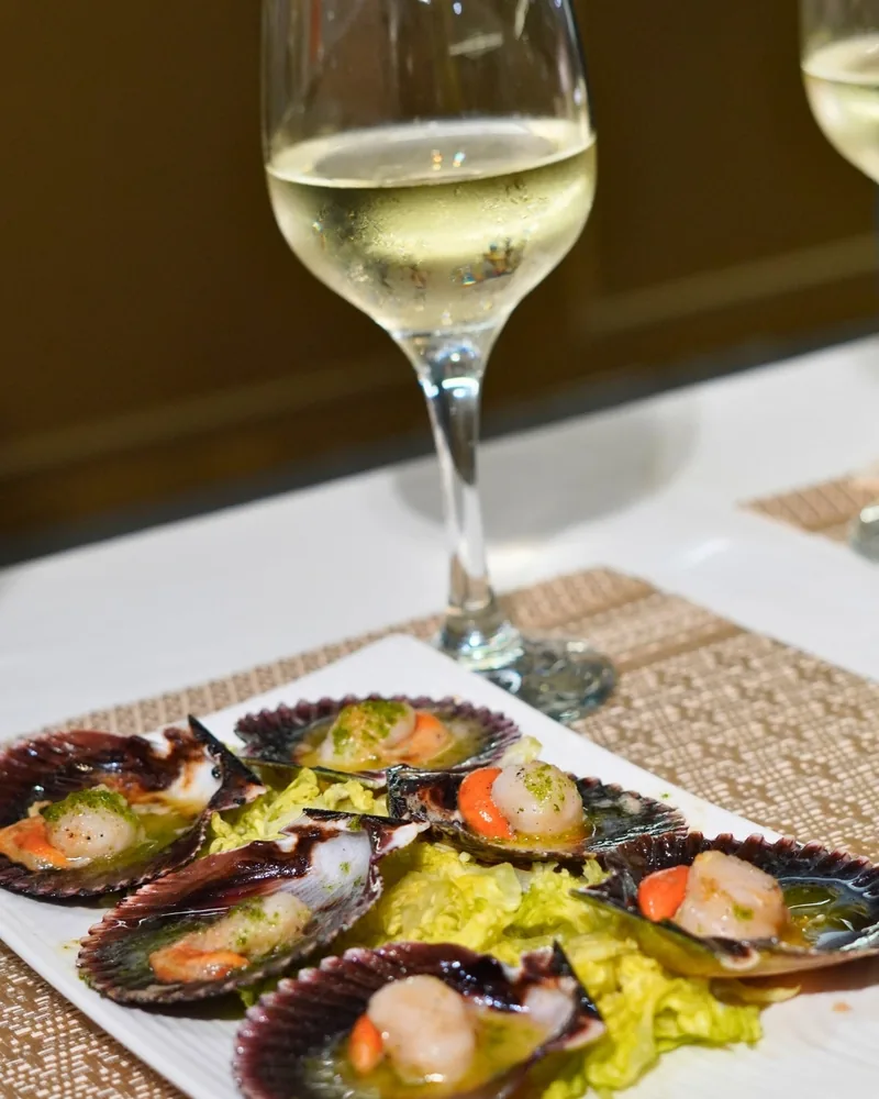 Zamburiñas a la plancha en una fuente, junto a una copa de vino blanco