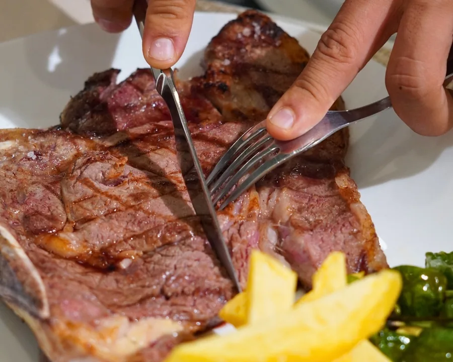 A chargrilled entrecôte being cut on the plate, with chips