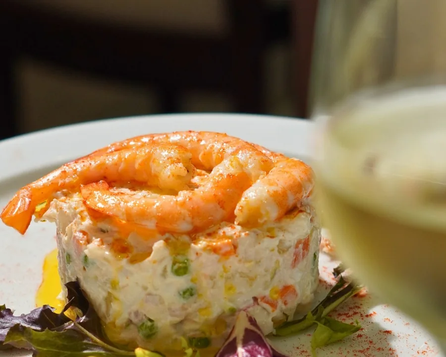 Una ensaladilla rusa con una corona de langostinos, en un plato blanco