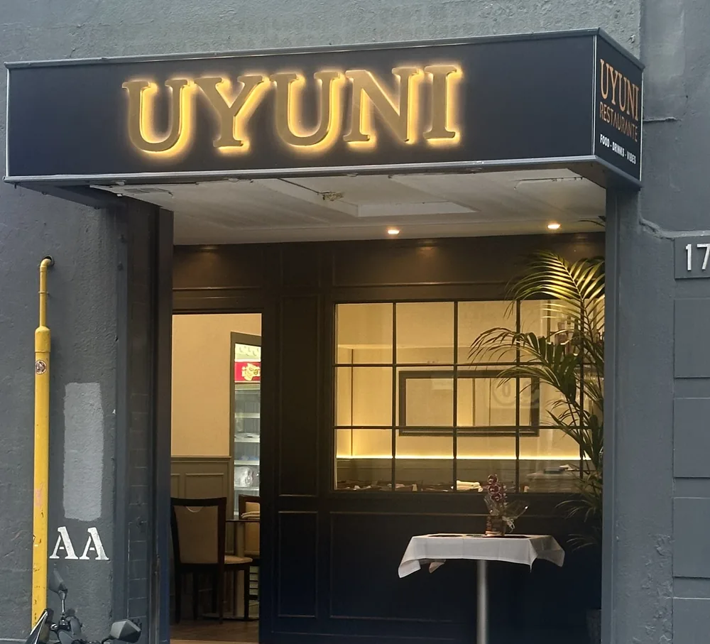 La entrada de UYUNI de noche, en el Carrer de Mèxic, 17: el rótulo encendido, la puerta y el ventanal
