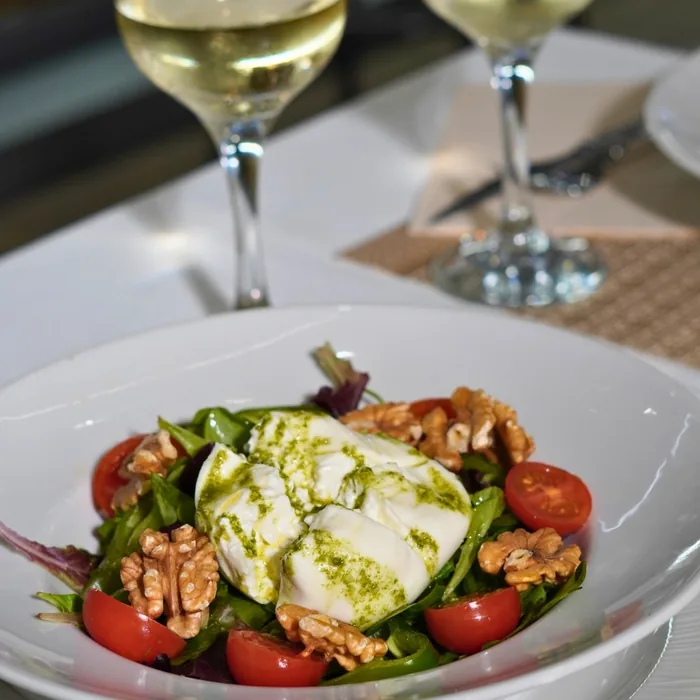 Una ensalada de burrata con tomate, nueces y brotes