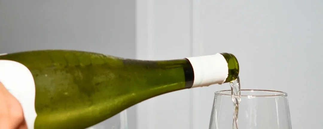 Una copa de vino blanco, sirviéndose junto a una fideuá