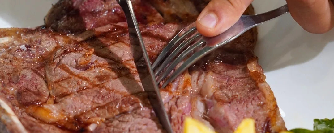 Un entrecot a la brasa, cortándose en el plato, con patatas fritas